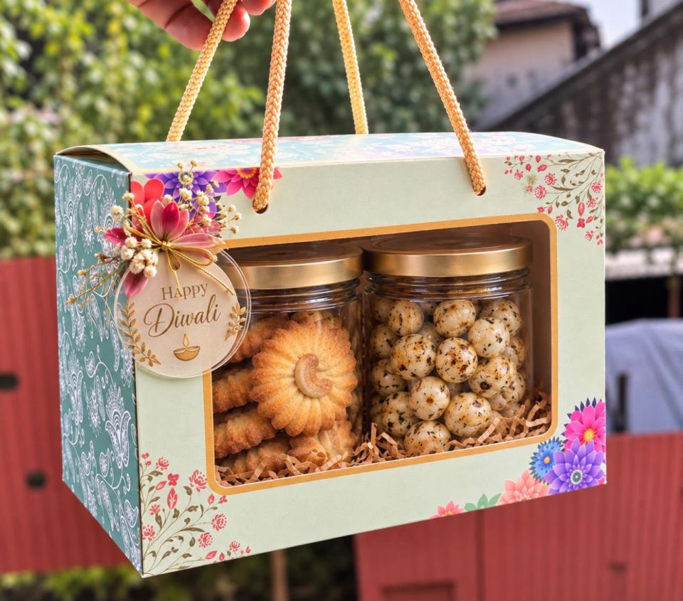 Window gift bag with rope handles, holding a jar of cashew-topped cookies and a jar of flavoured makhanas, with a Happy Diwali tag