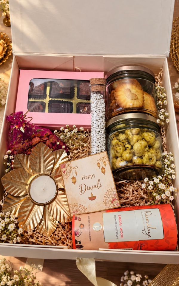 Cream gift box with a pink box of six chocolates, a mukhwas test tube, jars of cookies and makhanas, a potli, a gold flower diya, sandalwood dhoop sticks and a Happy Diwali card